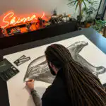 L'artiste Skima vu de dos en train de dessiner l'ours Pompon